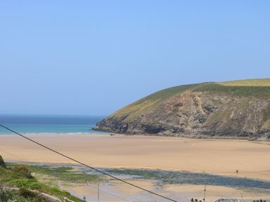 A sandy beach with a rocky cliff and ocean in the background at Seaport Lodge in Mawgan Porth