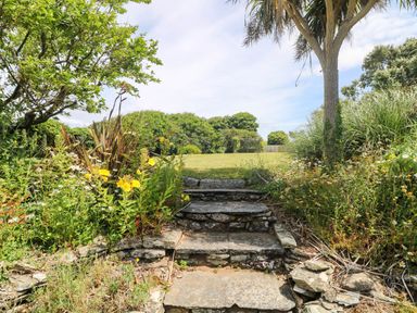 A garden with a stone pathway leading to a grassy area at Seaport Lodge in Mawgan Porth
