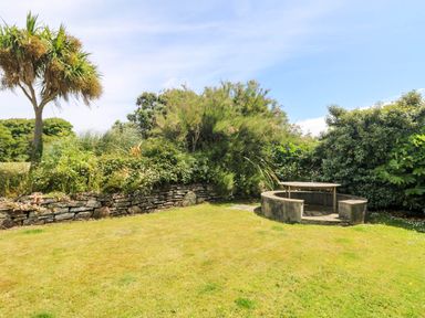 A garden with a stone bench and trees at Seaport Lodge in Mawgan Porth