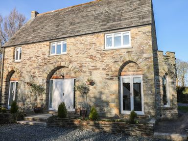 A stone house with arched doorways and windows with plants in pots outside at Lost Barn in Watergate Bay