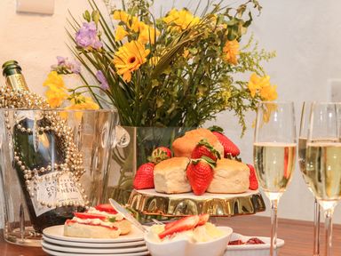 A table with a champagne bottle in an ice bucket beside scones with strawberries and cream and two glasses of champagne at Lost Barn in Watergate Bay