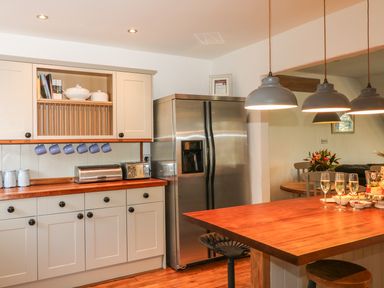 A kitchen with white cabinets a stainless steel refrigerator wooden countertop and hanging pendant lights at Lost Barn in Watergate Bay