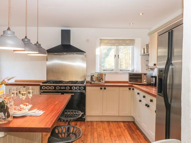 A kitchen with wooden countertops and white cabinets a black stove under a vent hood a stainless steel refrigerator and a small window at Lost Barn in Watergate Bay