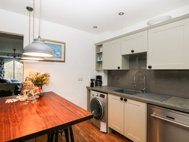 A kitchen with a wooden island, hanging lights, washing machine, sink, and cabinets at Lost Barn in Watergate Bay
