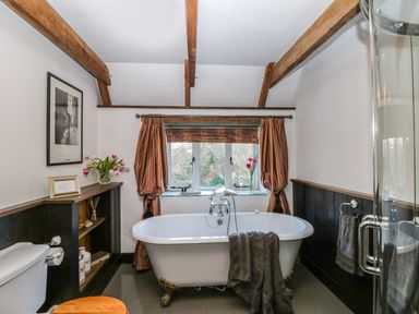 A bathroom with a clawfoot bathtub in front of a window with curtains and a toilet nearby at Lost Barn in Watergate Bay