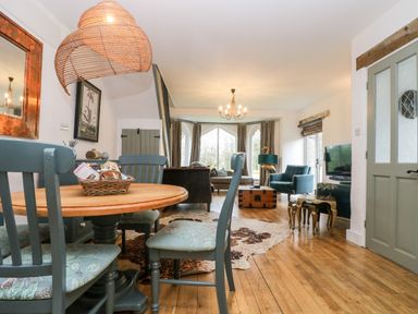 A dining area with a round table and chairs next to a living room with armchairs a sofa and a television at Lost Barn in Watergate Bay