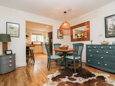 A dining room with a round wooden table and four chairs next to a blue dresser and a grey drawer unit at Lost Barn in Watergate Bay