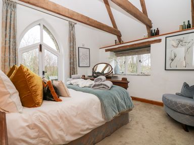 A bedroom with a bed pillows a blue blanket and a wooden dressing table under exposed wooden beams at Lost Barn in Watergate Bay