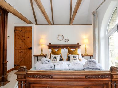 A bedroom with a wooden bed frame, two bedside tables with lamps, decorative pillows, and a wooden door at Lost Barn in Watergate Bay