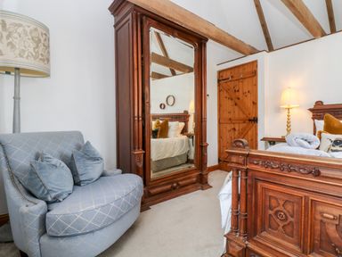 A bedroom with a wooden bed frame a large mirror wooden door and a blue chair with cushions at Lost Barn in Watergate Bay