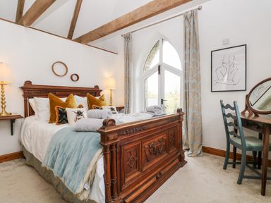 A bedroom with a carved wooden bed and blue blanket near arched window and dressing table at Lost Barn in Watergate Bay