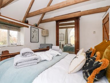 A bedroom with a wooden bed frame folded towels on the bed pillows a large mirror and exposed wooden beams at Lost Barn in Watergate Bay