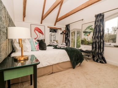 A bedroom with a bed side table lamp paintings and windows at Lost Barn in Watergate Bay