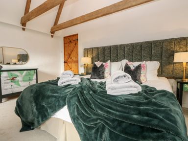 A bedroom with a large bed with green blanket and pillows wooden beams on ceiling and a dresser with a mirror at Lost Barn in Watergate Bay