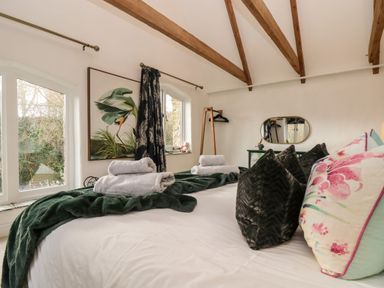 A bedroom with a bed with pillows and towels next to windows and wooden ceiling beams at Lost Barn in Watergate Bay