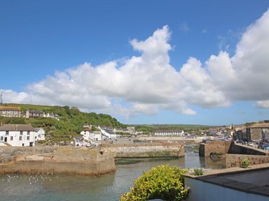 A harbor with stone walls and water surrounded by buildings and greenery under a partly cloudy blue sky at Courtyard in Nancegollan nr Porthleven