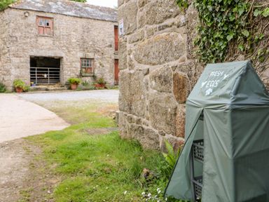 A stone farm building with a green covered stand labeled fresh eggs near a stone wall at Courtyard in Nancegollan nr Porthleven