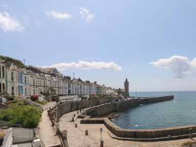 A coastal view with a row of houses along a curved stone seawall and a clock tower by the sea at Courtyard in Nancegollan nr Porthleven