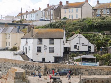 A stone pier with people walking near a white building named The Ship Inn and other houses in Courtyard in Nancegollan nr Porthleven