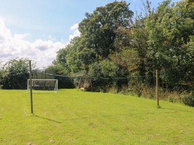 A grassy backyard with a small soccer goal a trampoline a wooden swing and trees at Courtyard in Nancegollan nr Porthleven