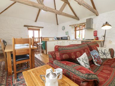 A kitchen and dining area with wooden beams on the ceiling and a red patterned couch at Courtyard in Nancegollan nr Porthleven