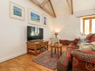 A living room with a patterned sofa wooden TV stand and framed pictures on the wall at Courtyard in Nancegollan nr Porthleven