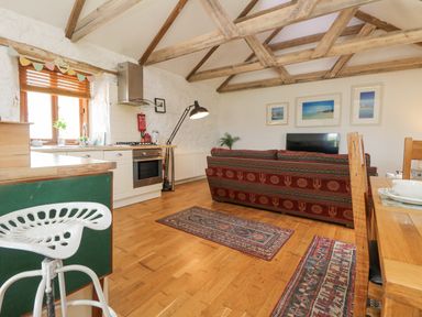 An open plan room with kitchen area and red patterned sofa in front of a television with wooden beams on the ceiling at Courtyard in Nancegollan nr Porthleven