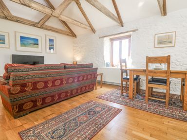 A living room with a patterned sofa, wooden dining table with chairs, rugs, and exposed wooden beams at Courtyard in Nancegollan nr Porthleven