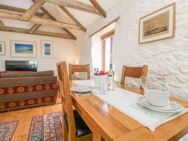 A dining table with chairs set with bowls plates and glasses next to a sofa and television in a living area at Courtyard in Nancegollan nr Porthleven