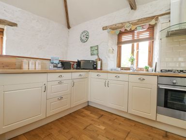 A kitchen with cream cabinets wooden countertops a window with wooden blinds a microwave a toaster and a built in oven at Courtyard in Nancegollan nr Porthleven