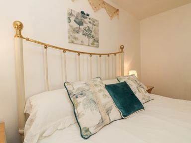 A bedroom with a brass and cream metal bed frame white bedding and decorative pillows with a nature pattern at Courtyard in Nancegollan nr Porthleven