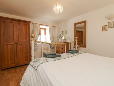 A bedroom with a bed, wooden wardrobe, chest of drawers, chair, window with curtains and a large wall mirror at Courtyard in Nancegollan nr Porthleven