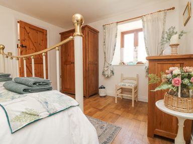 A bedroom with a bed folded towels a wooden wardrobe chair and a small table with flowers at Courtyard in Nancegollan nr Porthleven