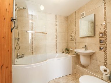 A bathroom with a bathtub shower combination a wall-mounted sink a mirror and tiled walls at Courtyard in Nancegollan nr Porthleven