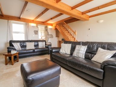A living room with two black leather sofas cushions a wooden side table and exposed wooden beams at Boslow in St Just