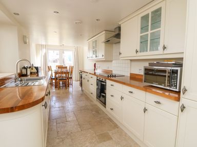 A kitchen with wooden countertops white cabinets a stainless steel microwave a sink and a dining table with chairs at Boslow in St Just