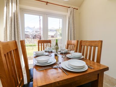 A dining table set with white dishes and wine glasses in a room with wooden chairs and glass doors at Boslow in St Just