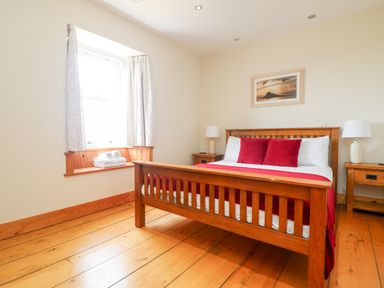 A bedroom with a wooden bed and two red pillows wooden floor and a window with white curtains at Boslow in St Just