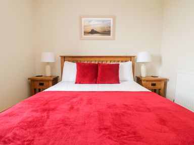 A bedroom with a wooden double bed red blanket and pillows two wooden bedside tables with lamps and a framed photo on the wall at Boslow in St Just