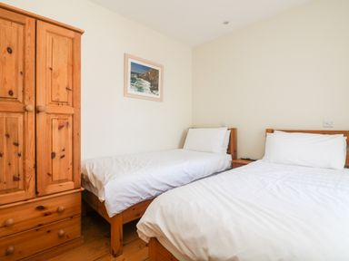 A bedroom with two single beds a wooden wardrobe and a framed picture on the wall at Boslow in St Just