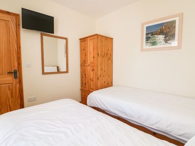 A bedroom with two single beds a wooden wardrobe a wall mirror a wall mounted television and a framed picture at Boslow in St Just