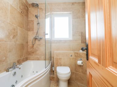 A bathroom with a bathtub shower combination a toilet and a wooden door at Boslow in St Just