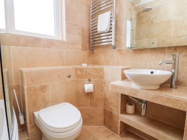 A bathroom with a toilet a sink a mirror a towel rack and tan tiles at Boslow in St Just