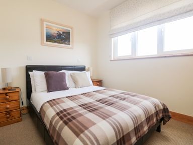 A bedroom with a bed covered with a plaid blanket and two bedside tables each with a lamp at Boslow in St Just