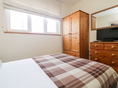 A bedroom with a bed covered by a plaid blanket a wooden wardrobe and a wooden dresser with a television on top at Boslow in St Just