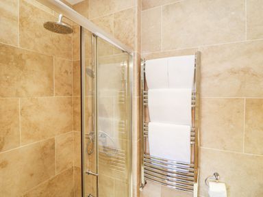 A shower with glass door a chrome towel rack holding white towels and a toilet paper holder in a bathroom at Boslow in St Just