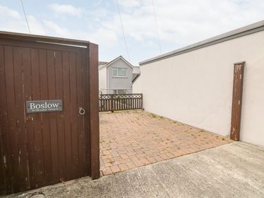 A paved driveway enclosed by walls and a wooden gate with a sign saying Boslow in St Just