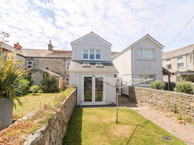 A backyard with grass a clothes drying rack stone walls and a two story white house at Boslow in St Just