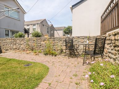 A garden patio area with two chairs and a table with a bottle and glasses next to a stone wall at Boslow in St Just