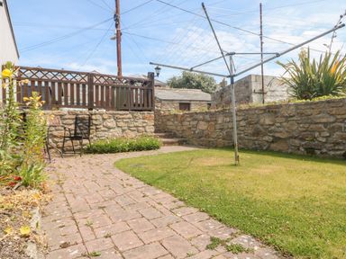 A garden with a rotary clothesline a brick pathway lawn chairs and stone walls at Boslow in St Just